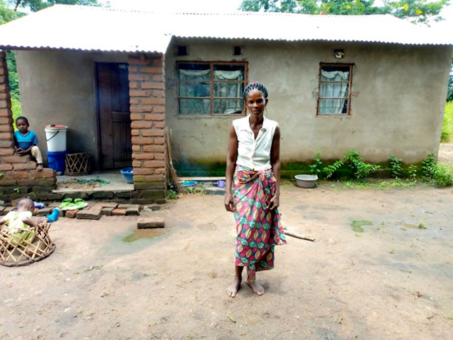 Elina stands in front of the house she built with loans from the Tilimbike Savings with Education Group ©ZACOP