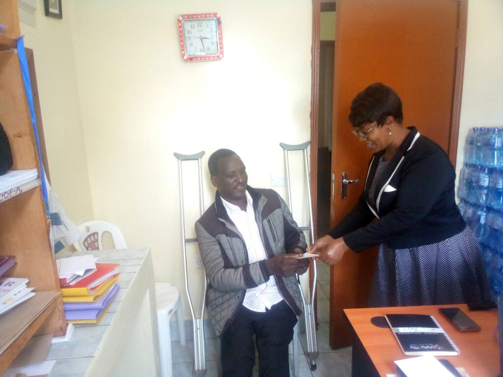 Gabriel receives his loan cheque from the Administrator of Eldoret’s Community Based Rehabilitation Centre, Rev’d Grace. © Diocese of Eldoret. Used with permission.