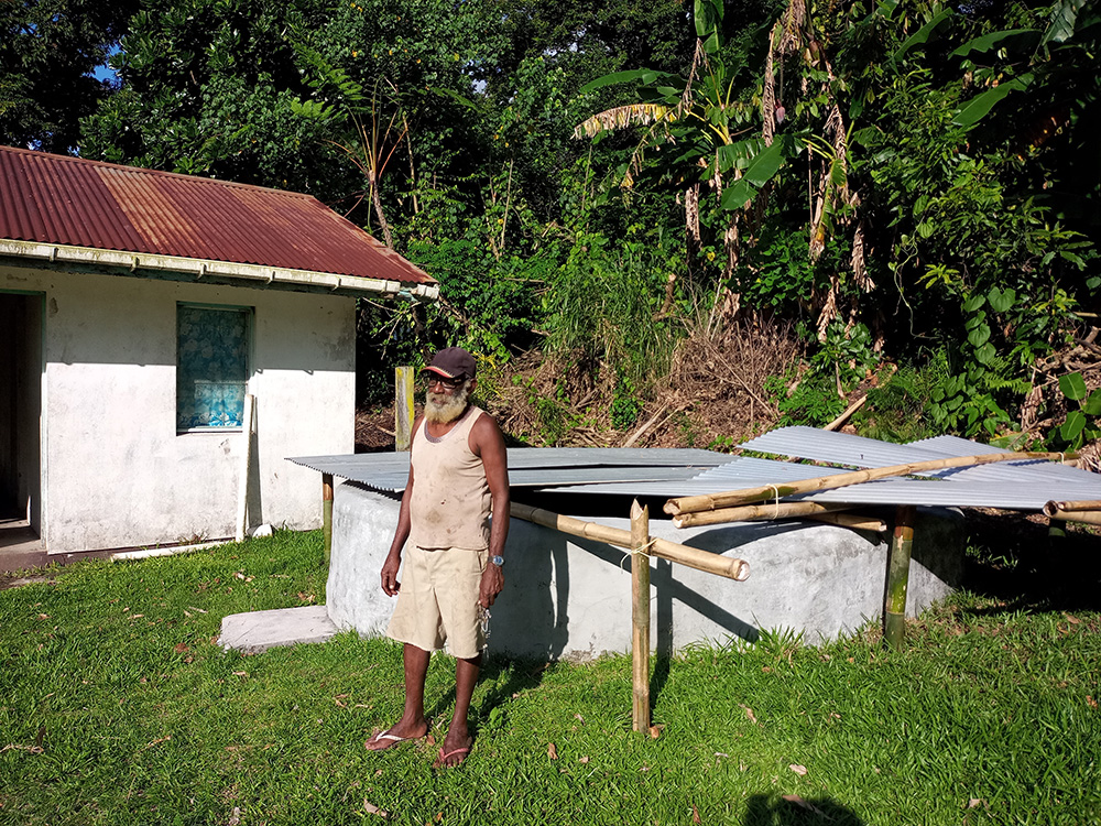 Hugh Blessing stands in front of the Nambangahake water tank built in 2021. © Terry Russell, AID.