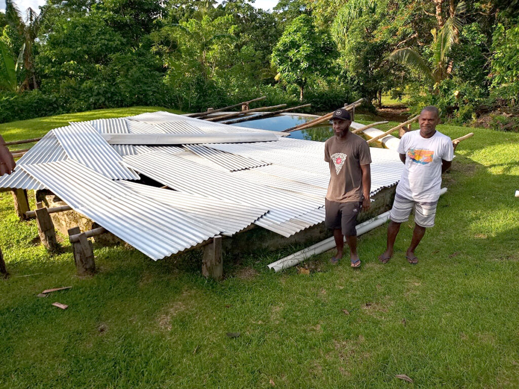 Edgel (right) with ACOM staff member, Bradley Tamata, standing next to the full reservoir. © ACOM Vanuatu. Used with permission.