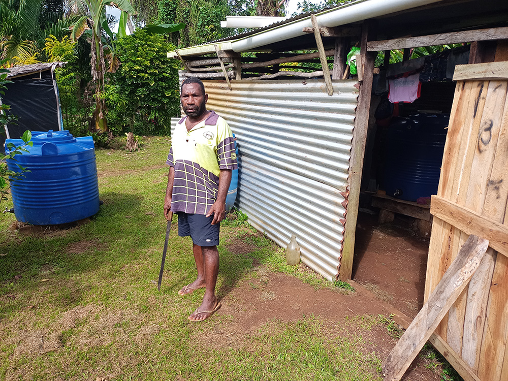 Fr Willie Loli, parish priest at Revelco on Santo Island in Vanuatu, with two 500-litre water tanks (one in the shed), both intended for use by people living with disabilities. © ABM/ Terry Russell.