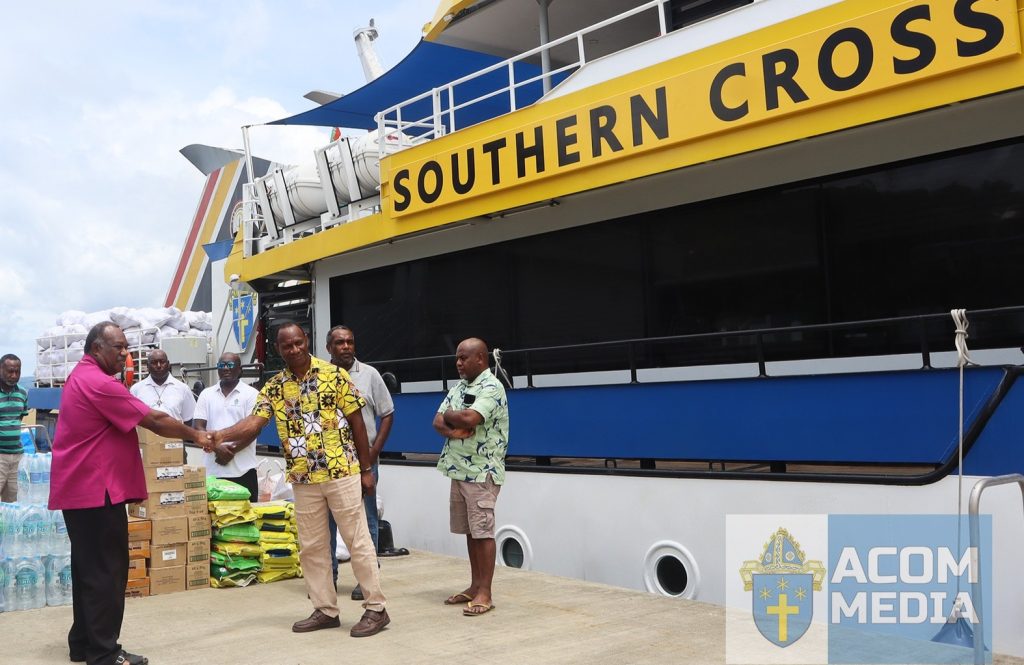 A ship, the Southern Cross, preparing to depart a Vanuatu dock. Men are shaking hands in front of it.