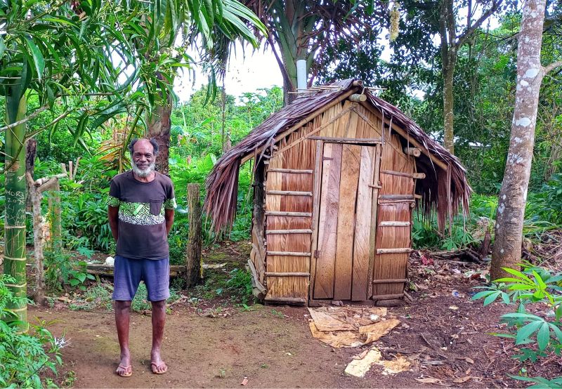 In Vanuatu, Charles stands outside a new toilet facility, which is improving health and hygiene in this community © ACOM Vanuatu. Used with permission.