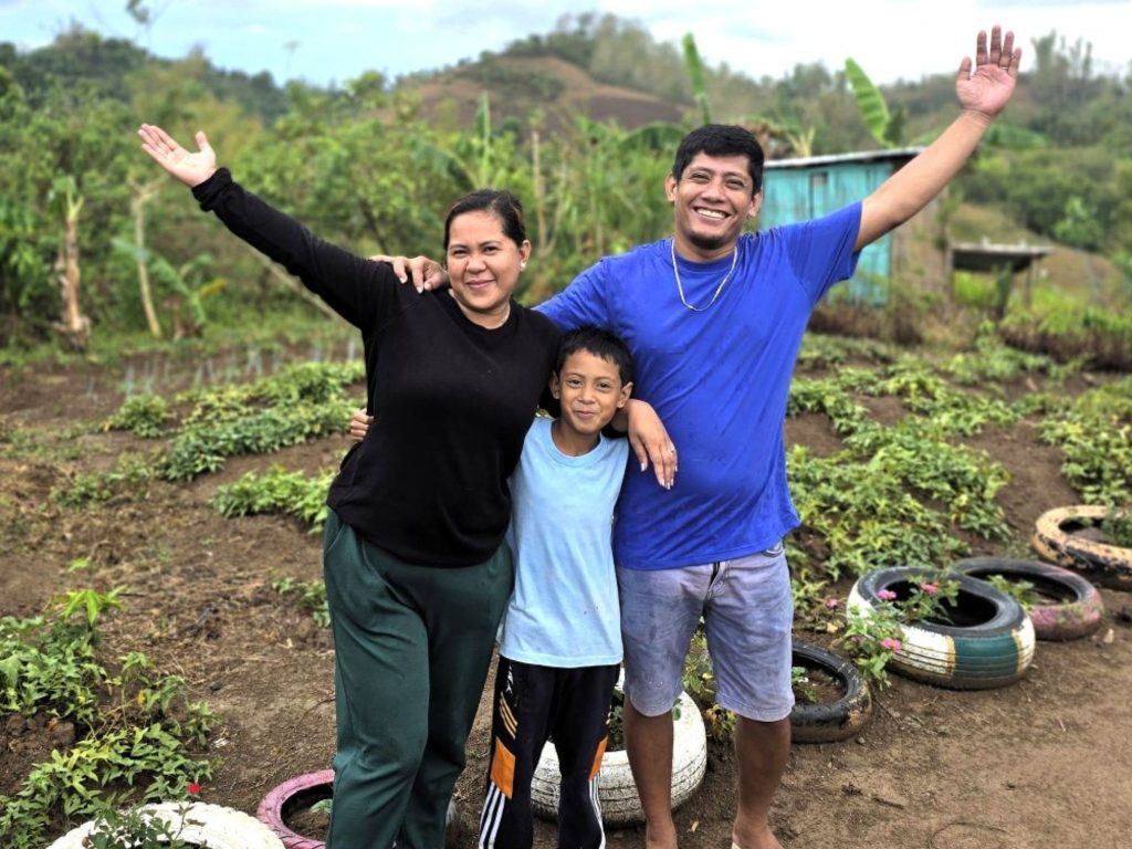 Thank You 2026 - a woman, man and boy from the Philippines hold out their arms in front of a planted field